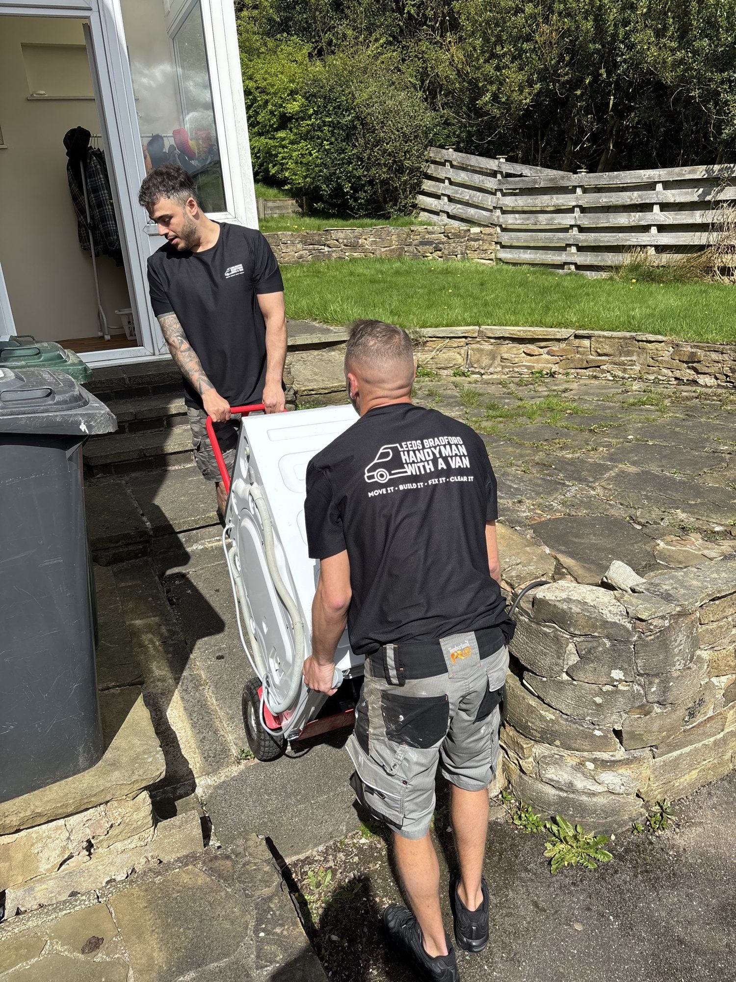 Crew wheeling a washing machine out of a house on a sack truck
